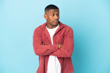 Mavi arka planda izole edilmiş genç latin adam yan tarafa bakıyor.