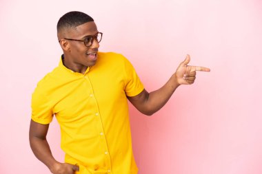 Pembe arka planda izole edilmiş genç latin adam parmağını yana doğru uzattı ve bir ürün sundu.