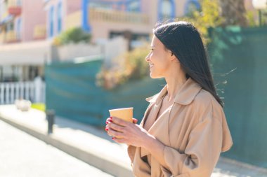 Açık havada elinde kahve tutan genç bir kadın.