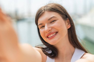 Genç, güzel bir kadın açık havada, mutlu bir ifadeyle.