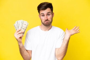 Kafkasyalı genç adam sarı arka planda izole edilmiş bir sürü para alıyor.