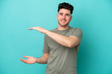 Genç beyaz adam mavi arka planda izole edilmiş bir ilan vermek için kopyalama alanı tutuyor.