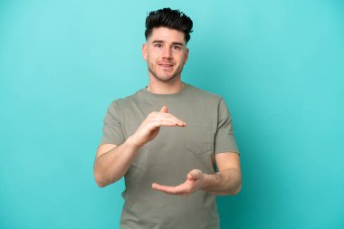 Mavi arka planda izole edilmiş genç beyaz adam bir ilan vermek için avucunun içinde hayali bir fotokopi makinesi tutuyor.