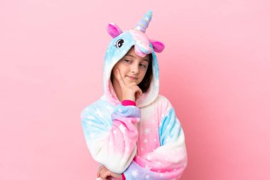 Tek boynuzlu pijama giyen beyaz bir kadın pembe arka planda izole edilmiş bir şekilde yukarı bakarken bir fikir düşünüyor.