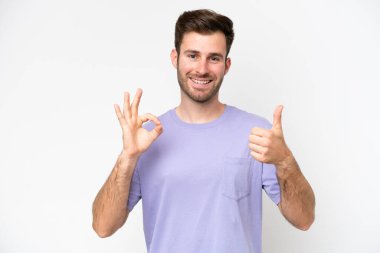 Beyaz arka planda izole edilmiş genç beyaz bir adam Tamam işareti ve baş parmak işareti