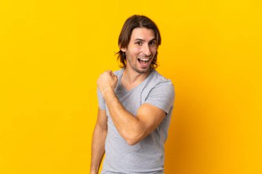 Sarı arka planda izole genç yakışıklı bir adam zaferi kutluyor.