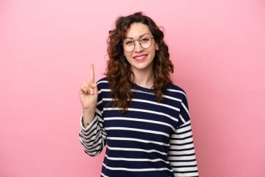 Pembe arka planda izole edilmiş genç beyaz kadın en iyinin işareti olarak parmağını kaldırıyor.