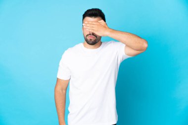 İzole edilmiş mavi arka plan üzerinde beyaz bir adam gözlerini elleriyle kapatıyor. Bir şey görmek istemiyorum.