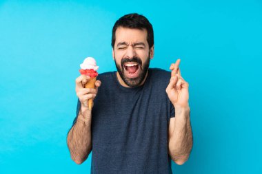 Kornet dondurması olan genç bir adam izole edilmiş mavi arka planda parmakları çapraz