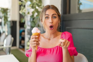 Açık havada kornet dondurması olan genç sarışın kadın şaşırmış ve ön tarafı işaret ediyor.