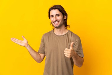 Sarı arka planda izole edilmiş genç bir adam. Avucunun içinde hayali bir şey tutuyor. Bir ilan vermek için.