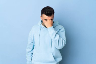 Kafkasyalı adam mavi arka planda, baş ağrısı var.