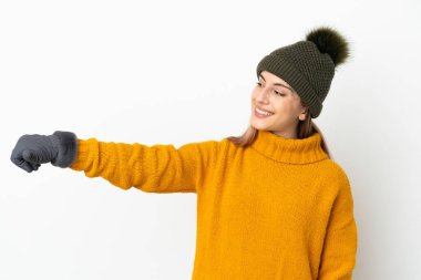 Beyaz arka planda izole edilmiş, kışlık şapkalı genç bir kız baş parmak hareketi yapıyor.