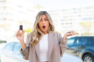 Güzel sarışın Uruguaylı kadın arabanın anahtarlarını açık havada tutuyor. Şaşırmış ve işaret ediyor.