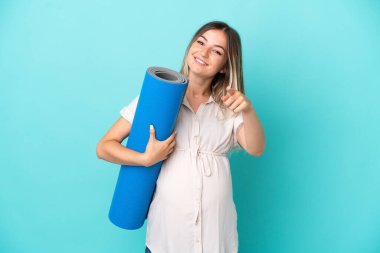 Genç Romen kadın mavi arka planda izole edilmiş hamile ve ön tarafı göstererek yoga derslerine gidiyor