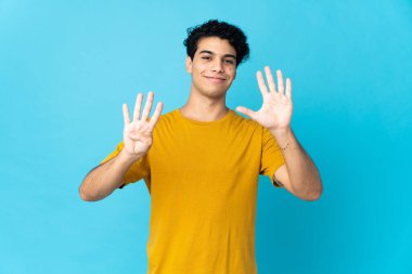 Genç Venezuelalı adam mavi arka planda izole edilmiş. Parmaklarıyla dokuz kişi sayıyor.