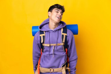 Sarı arka planda büyük bir sırt çantası olan genç dağcı gülüyor.