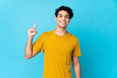 Genç Venezuelalı bir adam mavi arka planda izole edilmiş. Harika bir fikre işaret ediyor.