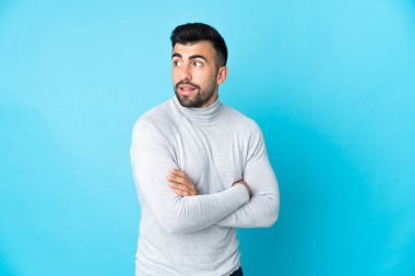 İzole edilmiş mavi arka planda beyaz bir adam yana bakıyor ve gülümsüyor.