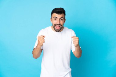 İzole edilmiş mavi arka plandaki beyaz adam galibiyeti kutluyor.