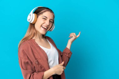 Genç beyaz kadın mavi arka planda izole edilmiş müzik dinliyor ve gitar hareketi yapıyor.