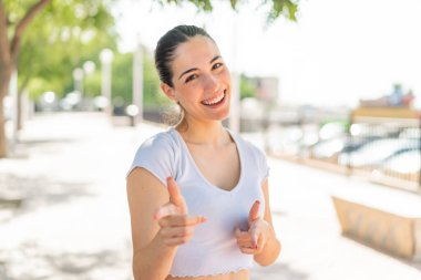 Açık havada genç ve güzel bir kadın ön tarafı gösteriyor ve gülümsüyor.