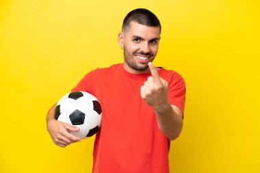 Sarı arka planda izole bir şekilde futbol oynayan beyaz bir adam geliyor.