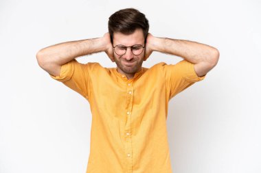 Beyaz arka planda izole edilmiş genç beyaz adam hayal kırıklığına uğramış ve kulaklarını kapatmış.