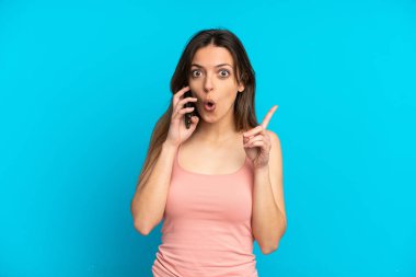 Mavi arka planda izole edilmiş cep telefonu kullanan beyaz bir kadın çözümü bulmak için parmağını kaldırıyor.