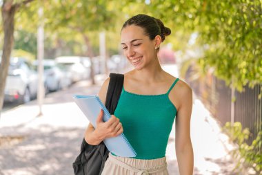 Açık havada, neşeli bir ifadeyle genç ve güzel bir bayan öğrenci.