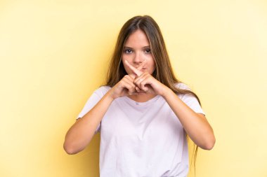 Sarı arka planda izole edilmiş genç beyaz kadın sessizlik işareti gösteriyor.