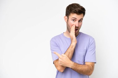 Beyaz arka planda izole edilmiş genç beyaz bir adam bir ürün sunmak ve bir şeyler fısıldamak için kenarı işaret ediyor.