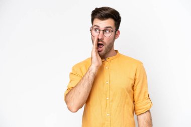 Beyaz arka planda izole edilmiş genç beyaz adam yan tarafa bakarken sürpriz bir jest yapıyor.