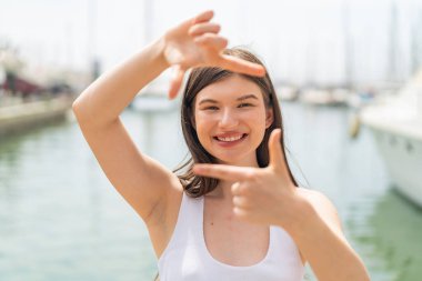 Genç, güzel bir kadın açık havada, mutlu bir ifadeyle.