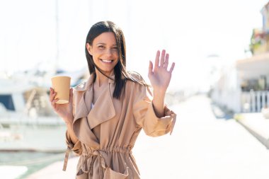 Dışarıdaki genç kadın elinde kahveyle dışarıda elini sallayarak mutlu bir ifadeyle selam veriyor.
