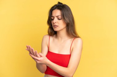 Sarı arka planda izole edilmiş genç beyaz kadın ellerinde acıdan kıvranıyor.