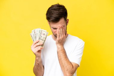 Kafkasyalı genç adam, sarı arka planda izole edilmiş, yorgun ve hasta bir ifadeyle bir sürü para alıyor.