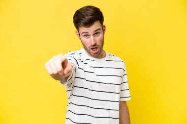 Sarı arka planda izole edilmiş genç beyaz adam hayal kırıklığına uğramış ve ön tarafı işaret ediyor.