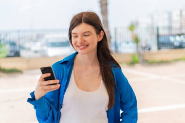 Genç, güzel Ukraynalı bir kadın açık havada mutlu bir ifadeyle cep telefonu kullanıyor.