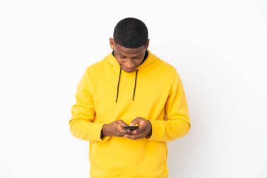 Beyaz arka planda izole edilmiş genç latin adam cep telefonuyla bir mesaj gönderiyor.