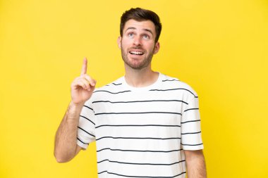 Sarı arka planda izole edilmiş genç beyaz adam yukarı bakıyor ve şaşırıyor.