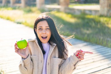 Açık havada elmalı genç bir kadın şaşırmış ve işaret ediyor.