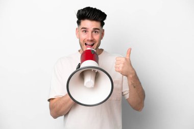 Beyaz arka planda izole edilmiş genç beyaz bir adam bir şey duyurmak için megafondan bağırıyor ve başparmağını kaldırıyor.