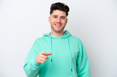 Beyaz arka planda izole edilmiş genç beyaz adam şaşırmış ve ön tarafı işaret ediyor.