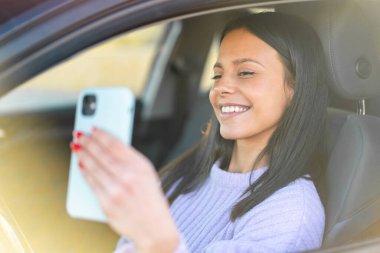 Dışarıdaki bir arabada cep telefonu kullanan genç bir kadın.