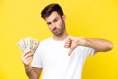 Kafkasyalı genç adam, sarı arka planda izole edilmiş bir sürü para alıyor.