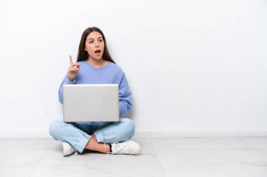 Yerde dizüstü bilgisayarlı beyaz bir kadın oturuyor. Beyaz arka planda izole edilmiş.