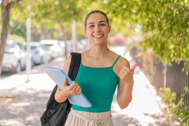 Açık havada genç ve güzel bir bayan bir ürün sunmak için kenarı işaret ediyor.