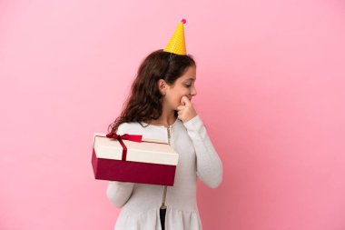 Küçük beyaz kız elinde pembe arka planda izole edilmiş bir hediye tutuyor. Bir fikir üretiyor ve bakıyor.