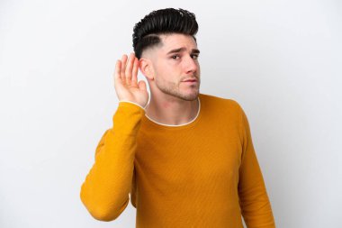 Beyaz arka planda izole edilmiş genç beyaz bir adam. Kulağına elini sürerek bir şeyler dinliyor.